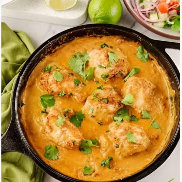 Chicken in a creamy orange sauce, garnished with fresh cilantro, in a black cast iron pan.