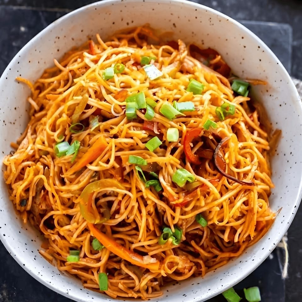 Close-up of a bowl of Hakka noodles with vegetables and spring onions.
