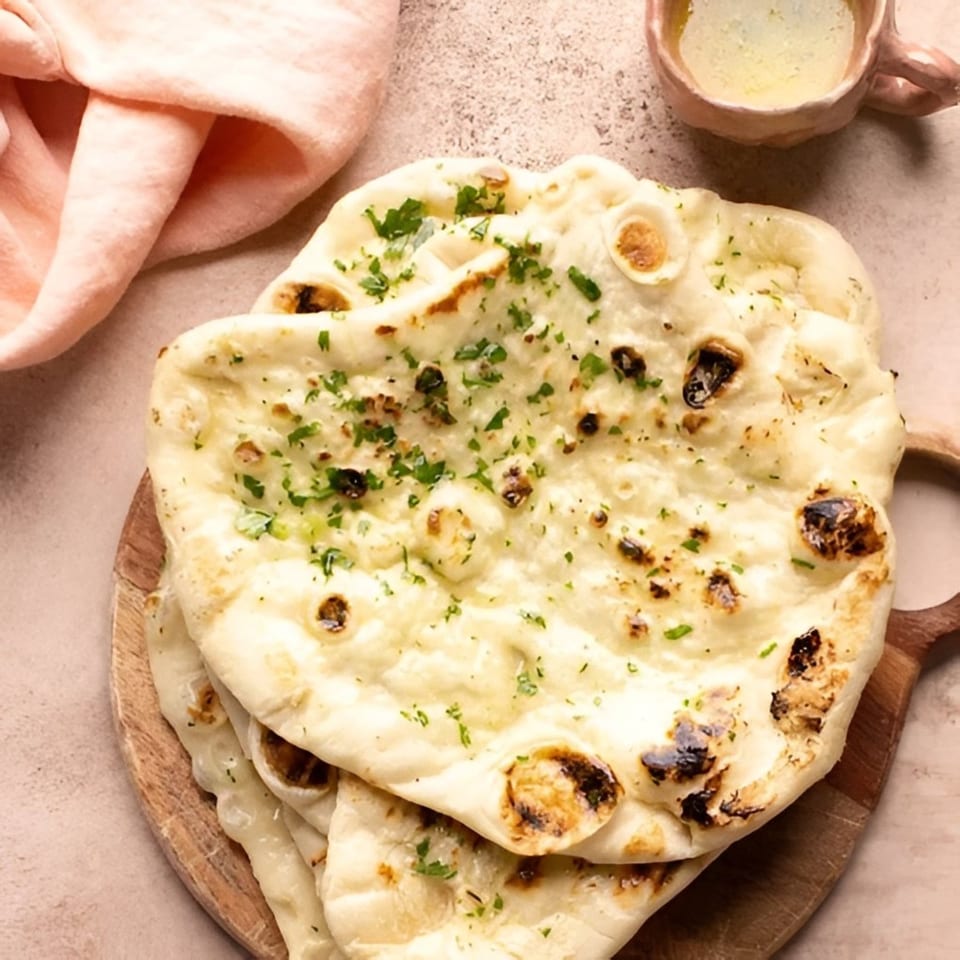 Stack of warm, fluffy naan bread with charred spots and fresh parsley, next to a small bowl of butter.