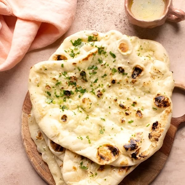 Stack of warm naan bread with fresh parsley on a wooden board, with a small cup of butter.